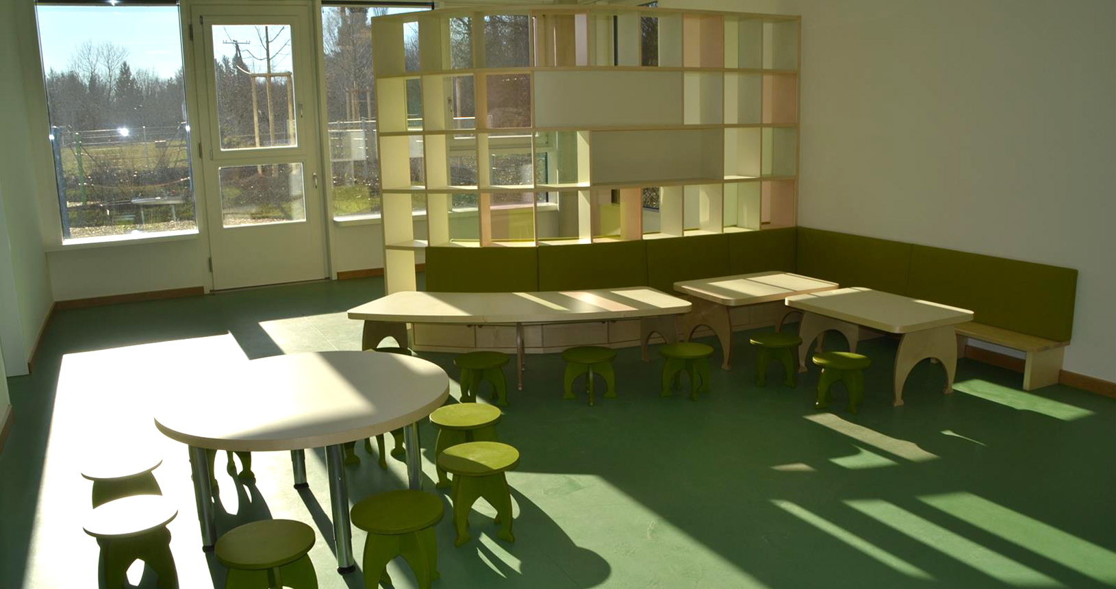 Kindergartenraum mit Regalsystem und kleinen Tischen und Stühlen